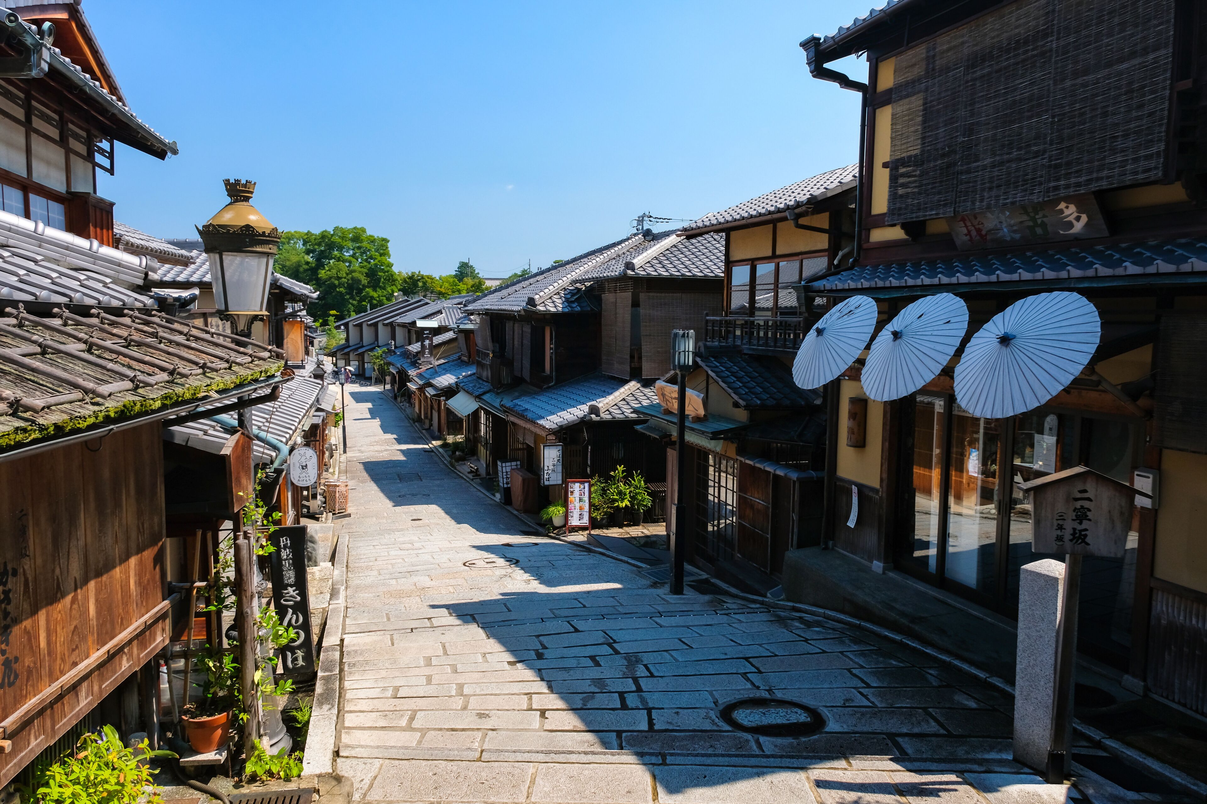 Uma rua tradicional japonesa com edifícios de madeira, calçada de pedra e guarda-chuvas decorativos.