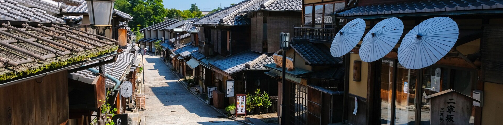 Uma rua tradicional japonesa com edifícios de madeira, calçada de pedra e guarda-chuvas decorativos.