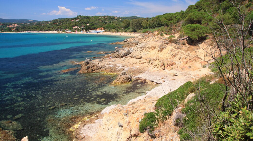 Un paysage côtier caractérisé par une eau turquoise limpide, des rivages rocheux et des collines verdoyantes en arrière-plan.