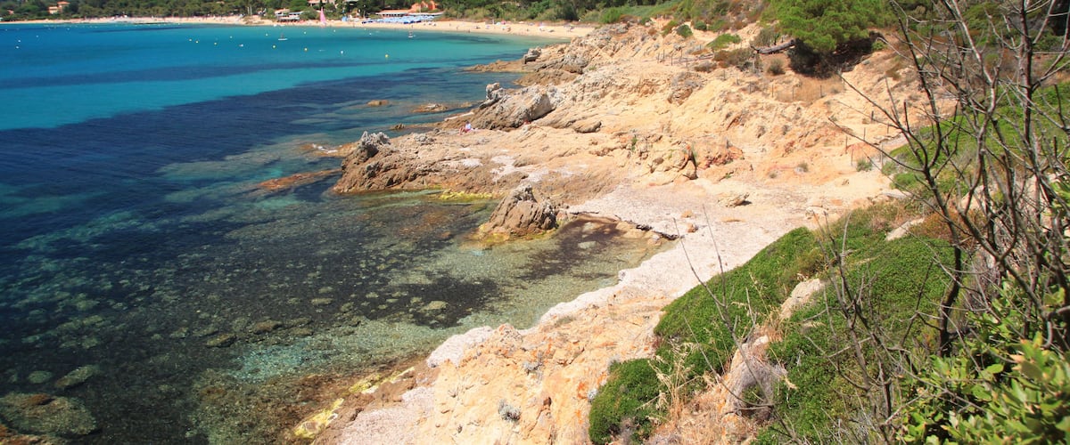 Un paysage côtier caractérisé par une eau turquoise limpide, des rivages rocheux et des collines verdoyantes en arrière-plan.
