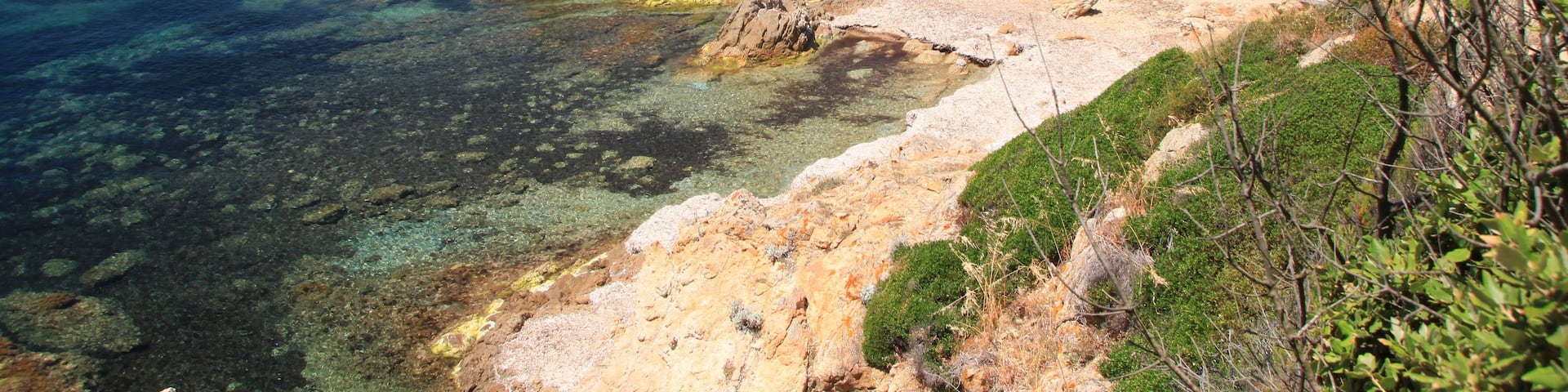 A coastal landscape with clear turquoise waters, rocky shores, and green hills in the background.
