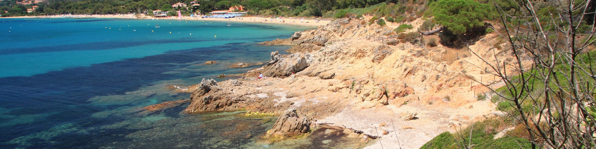 A coastal landscape with clear turquoise waters, rocky shores, and green hills in the background.