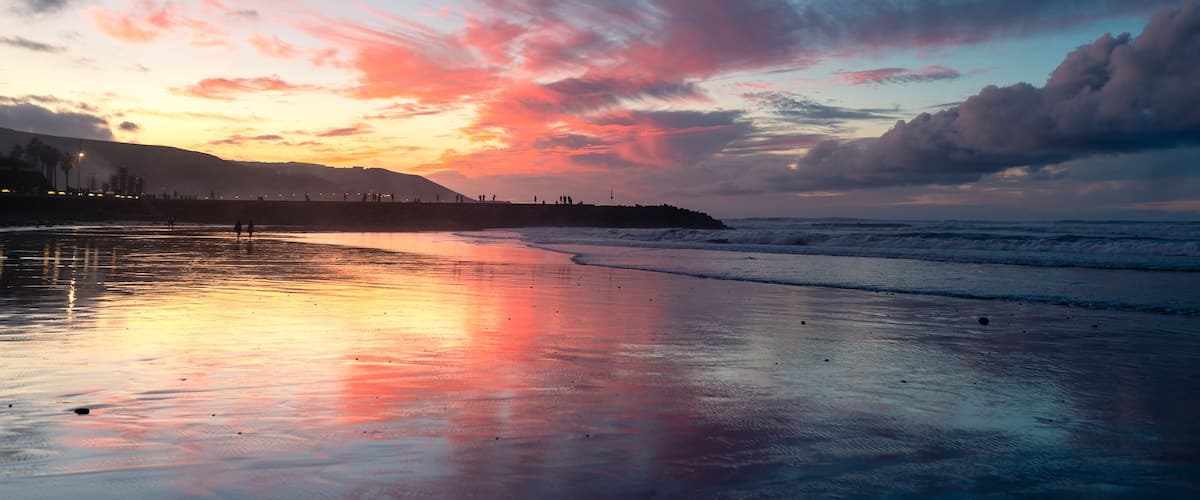 Uma praia ao pôr do sol, com céu colorido e ondas calmas.