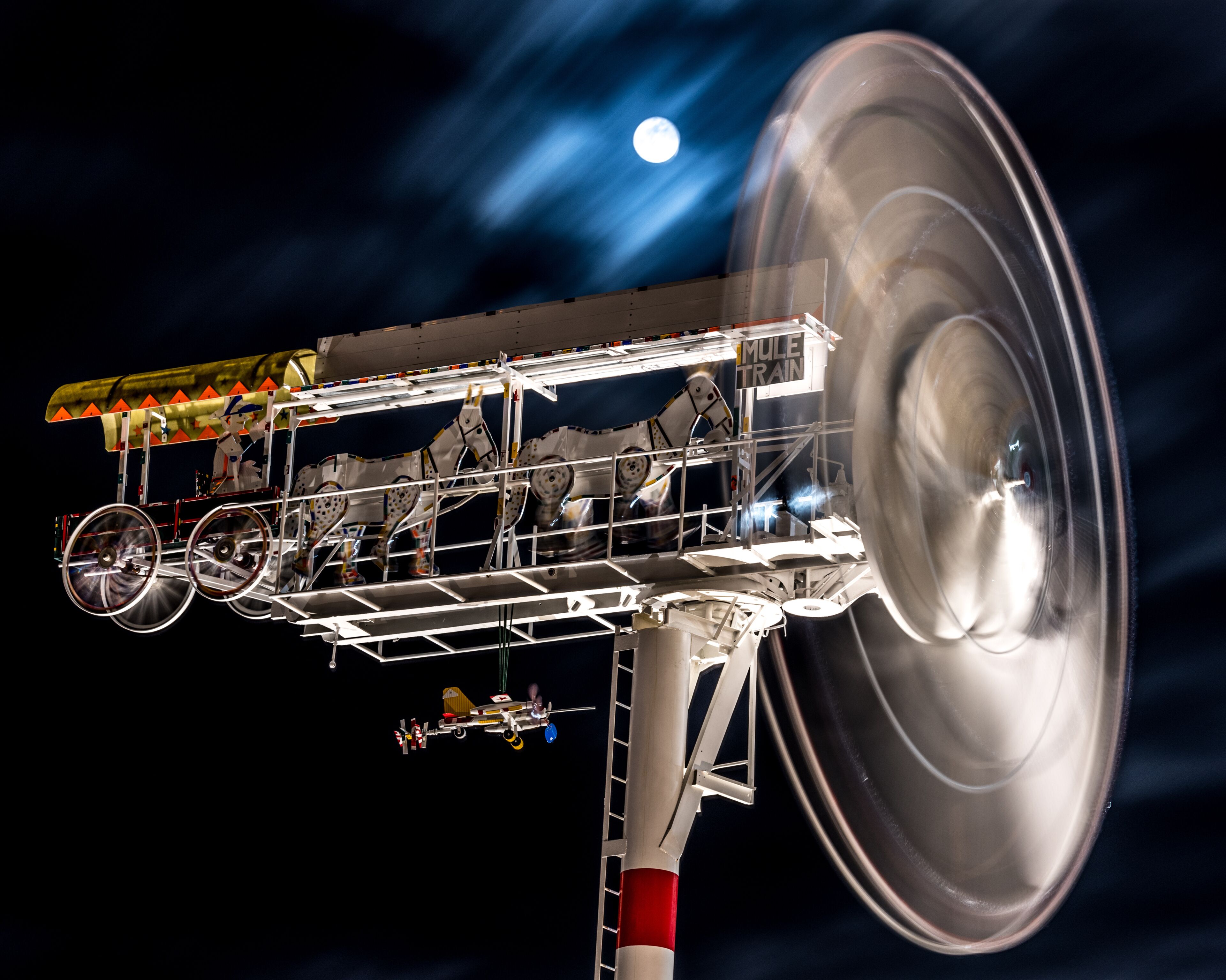 A whirligig spins at night in front of a full moon