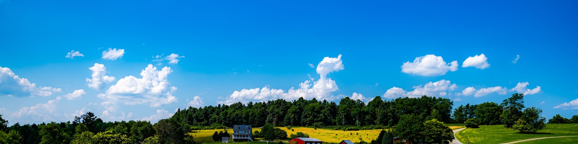 A rural landscape with a winding road, green fields, a red barn, and a blue house.