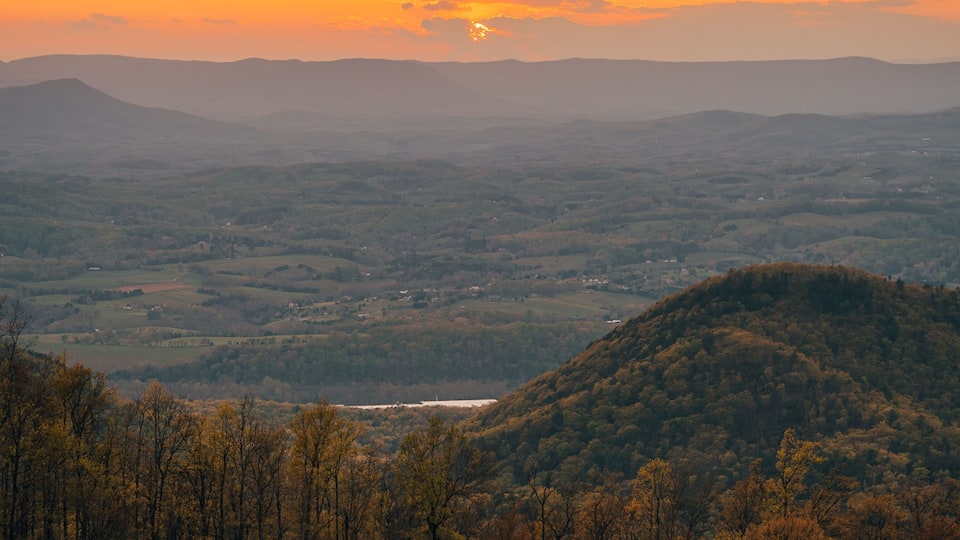 A sunset over a hilly landscape with a valley and a river.