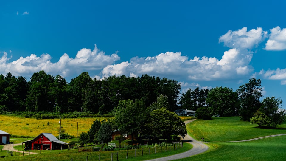 A rural landscape with a red barn, a winding road, and a house on a hill.