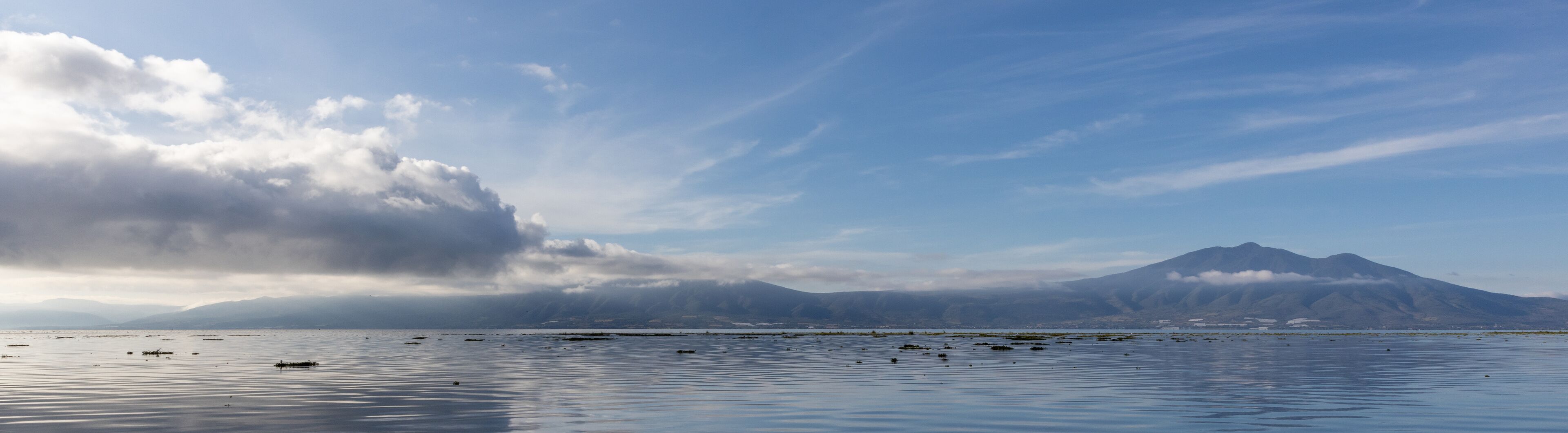 A calm lake with mountains in the background and a cloudy sky.