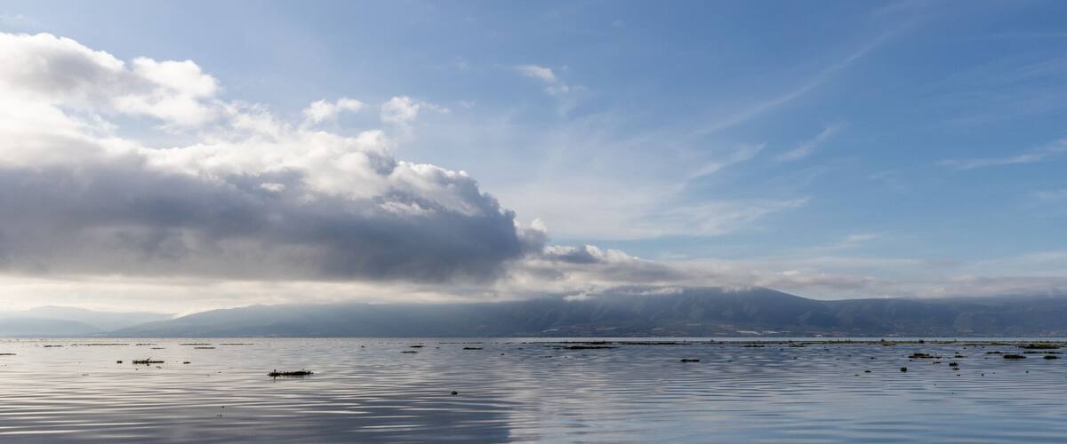 A calm lake with mountains in the background and a cloudy sky.
