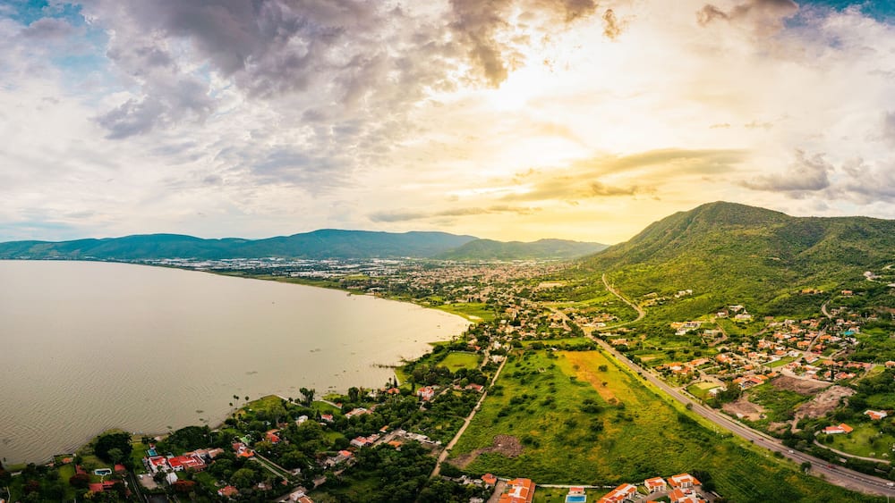 A panorama of mountains and lake with the sunset as background. Clouds and blue sky with trees and colors