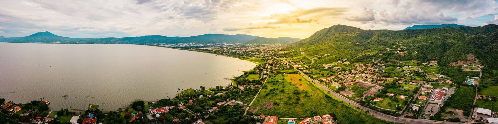 A panorama of mountains and lake with the sunset as background. Clouds and blue sky with trees and colors