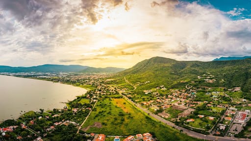 A panorama of mountains and lake with the sunset as background. Clouds and blue sky with trees and colors