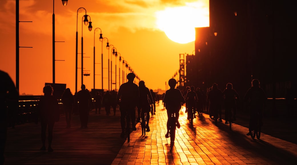 Large sun setting looking straight down a long boardwalk, with silhouettes of walkers and cyclists. Long Beach New York.