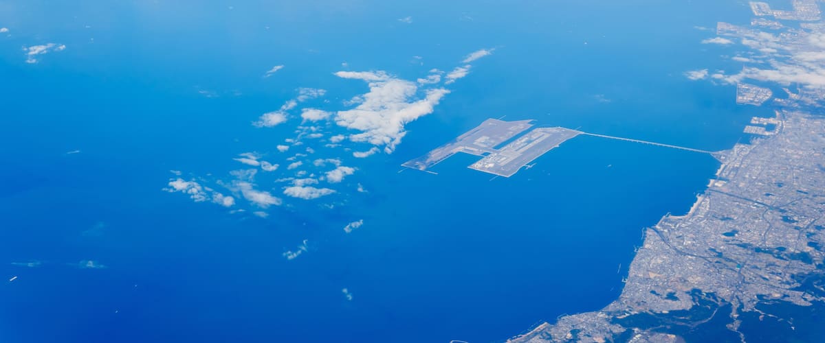 Et kystlandskab med et stort vandområde, en landingsbane og spredte skyer.