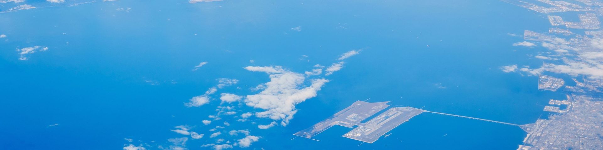 Un paysage urbain côtier avec une vaste étendue d’eau, une piste d’atterrissage et quelques nuages épars.