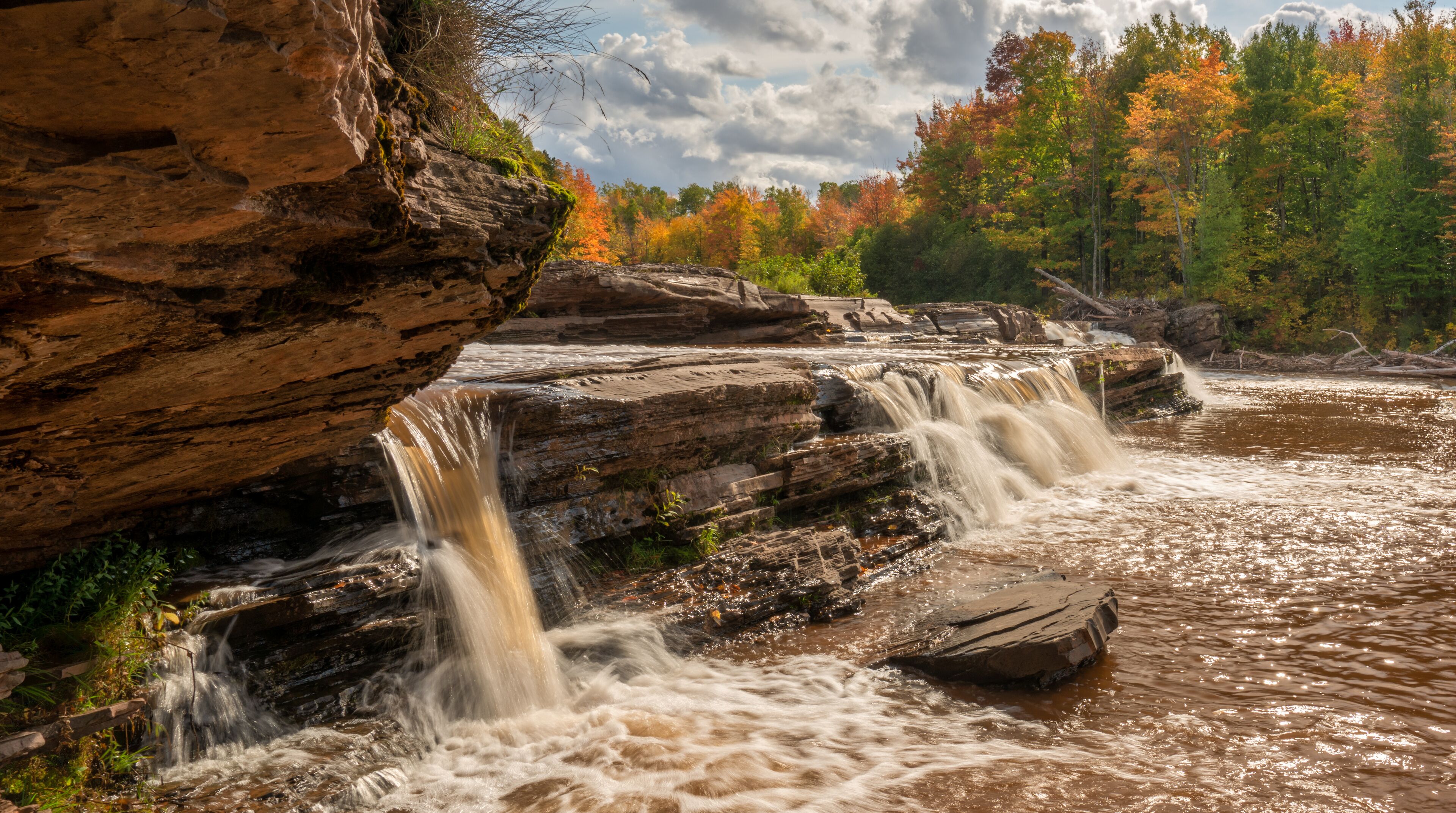 A waterfall cascading over rocky terrain with autumn foliage in the background.