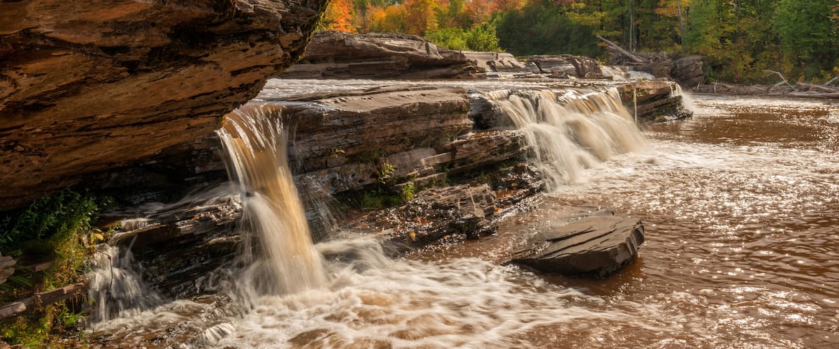 A waterfall cascading over rocky terrain with autumn foliage in the background.