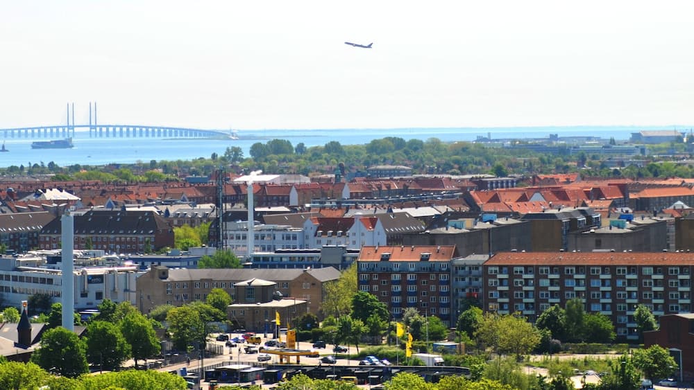 Une vue urbaine avec un pont imposant en arrière-plan, un mélange de bâtiments résidentiels et commerciaux, et un ciel dégagé.