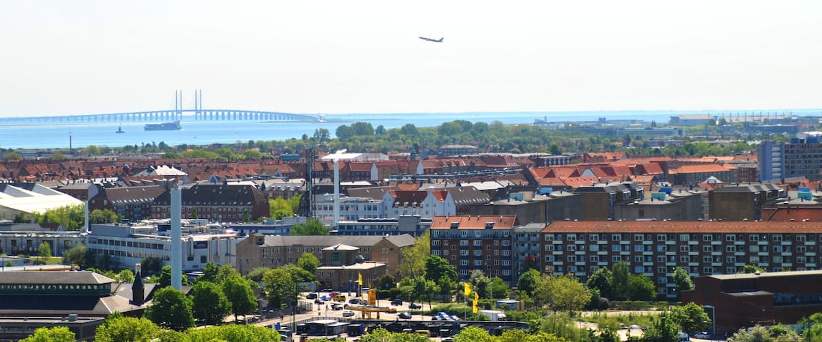 A cityscape with a prominent bridge in the background, a mix of residential and commercial buildings, and a clear sky.