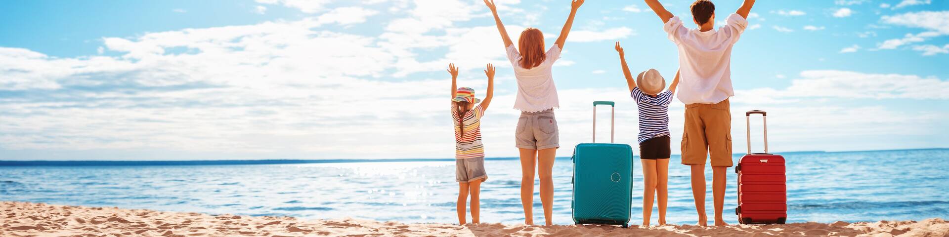 Mother and father with their children standing on the beach with suitcases.