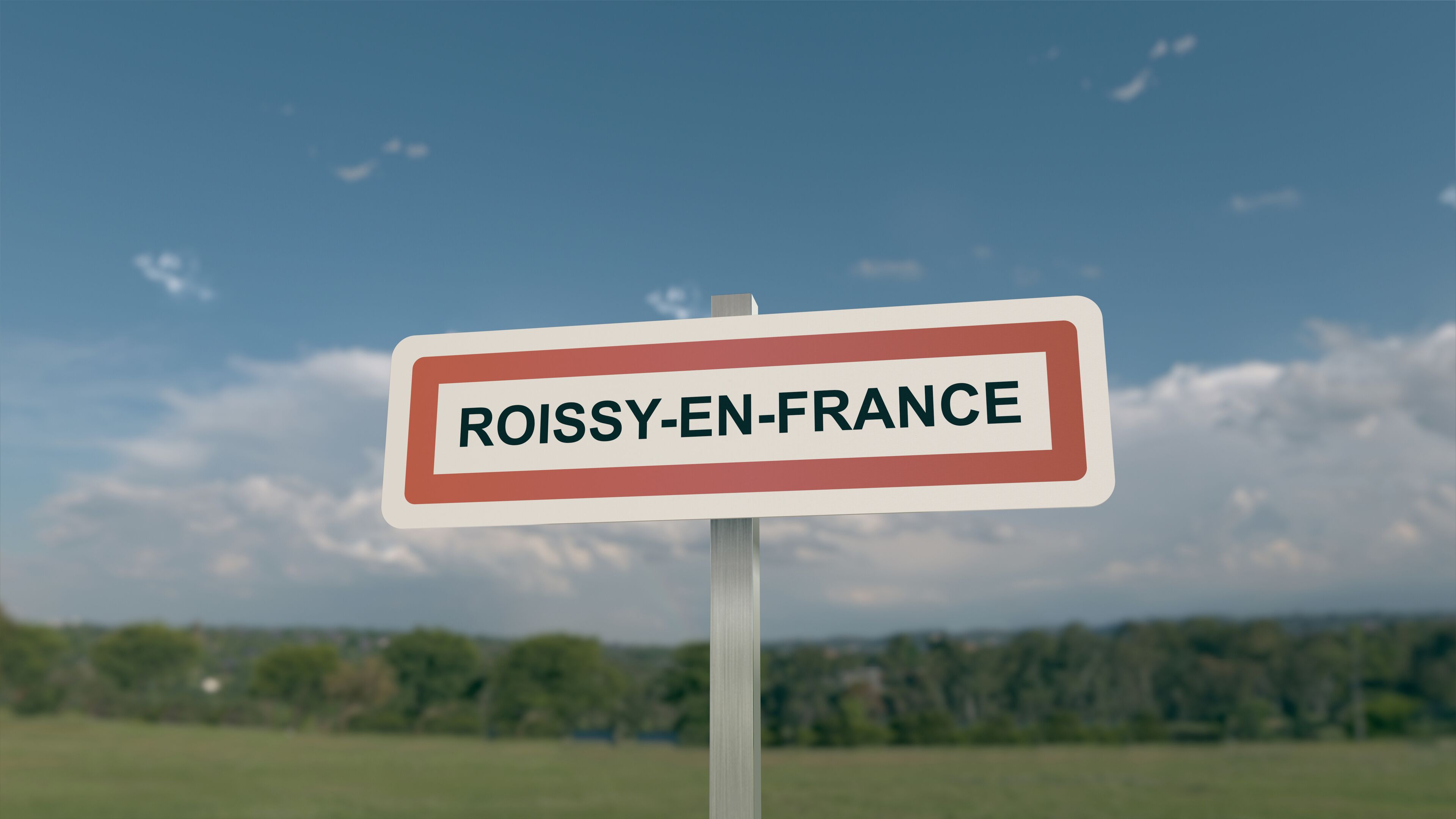 A sign with the text "ROISSY-EN-FRANCE" against a clear blue sky with scattered clouds.