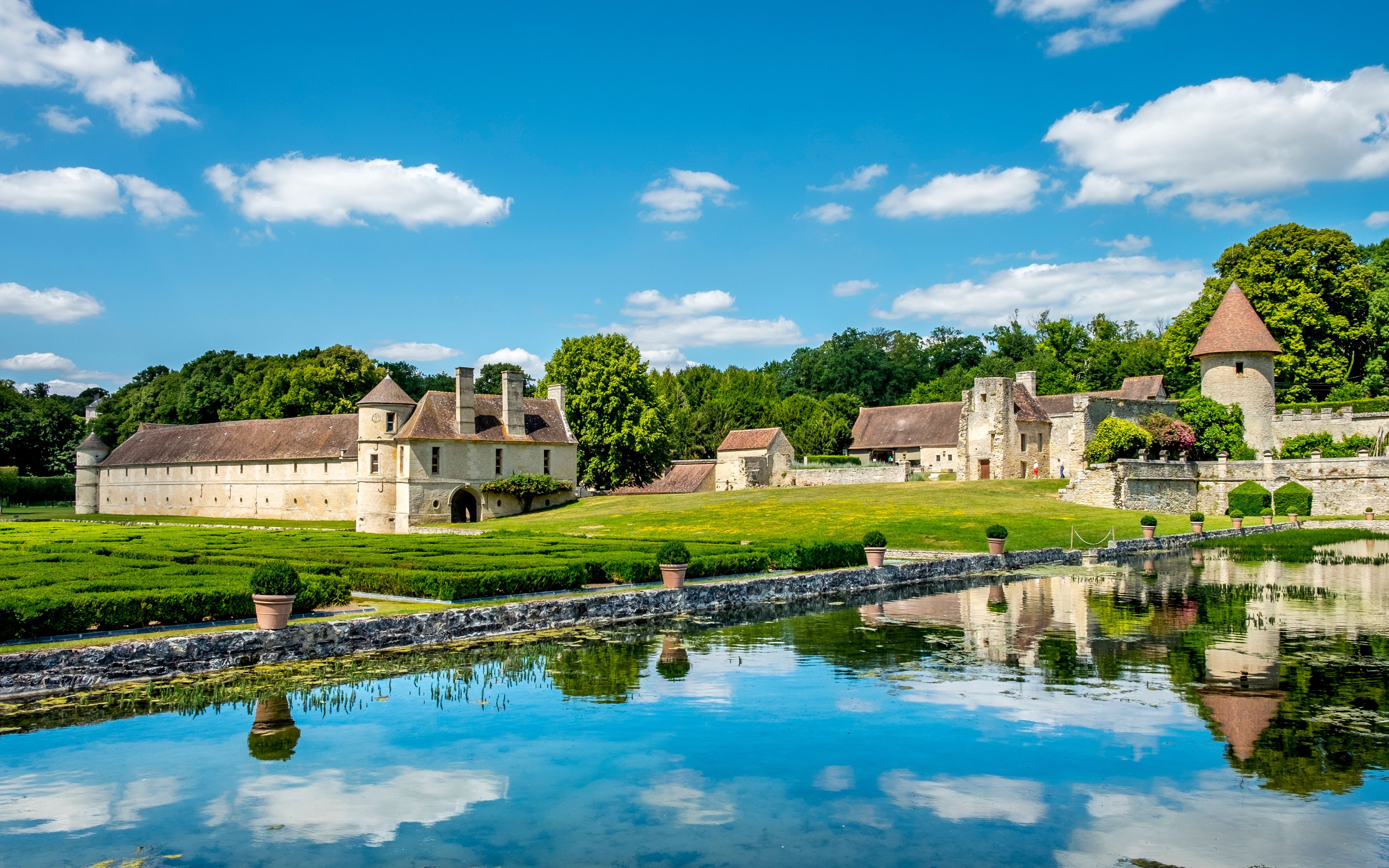 A historic estate with a moat, reflecting buildings, and lush greenery.