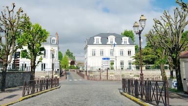 Rua de paralelepípedos que leva a um prédio branco com uma placa indicando direções para Paris e outros destinos locais.