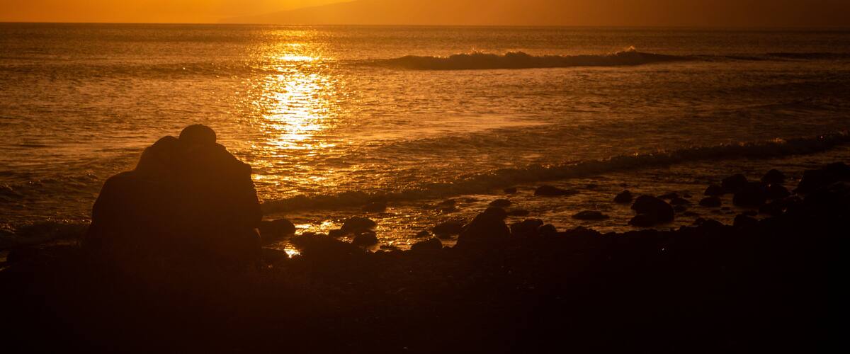 A sunset over the ocean with a silhouette of rocks in the foreground.