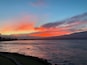 Un atardecer sobre un mar tranquilo con un litoral rocoso y montañas distantes.