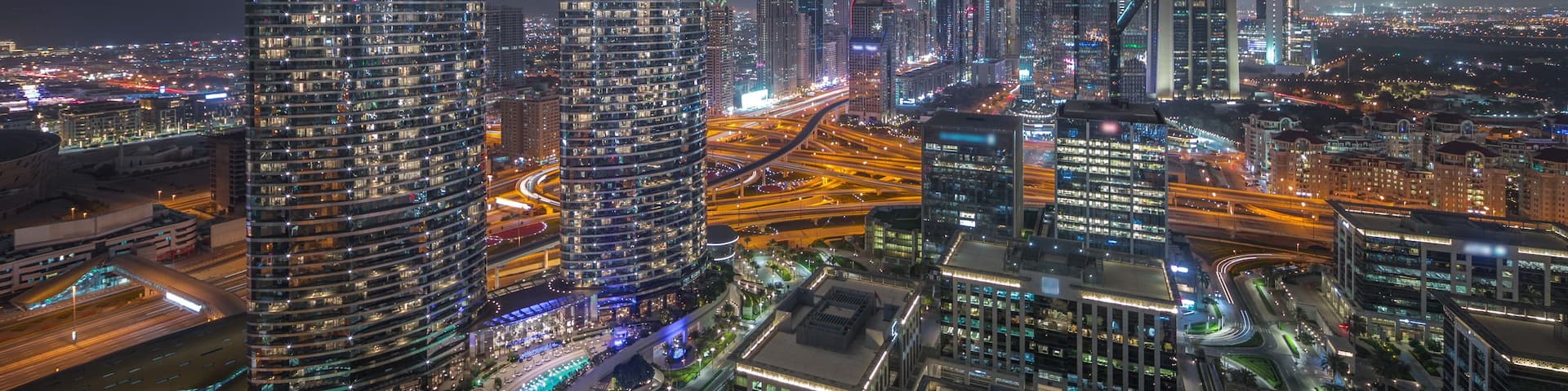 A nighttime cityscape with illuminated skyscrapers and a busy highway.