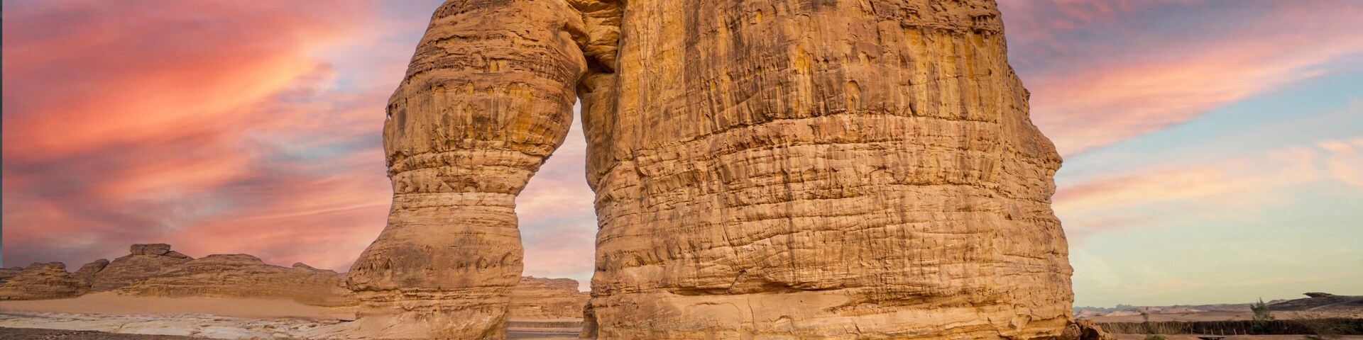 Una gran formación rocosa con un arco natural, rodeada de paisaje desértico.