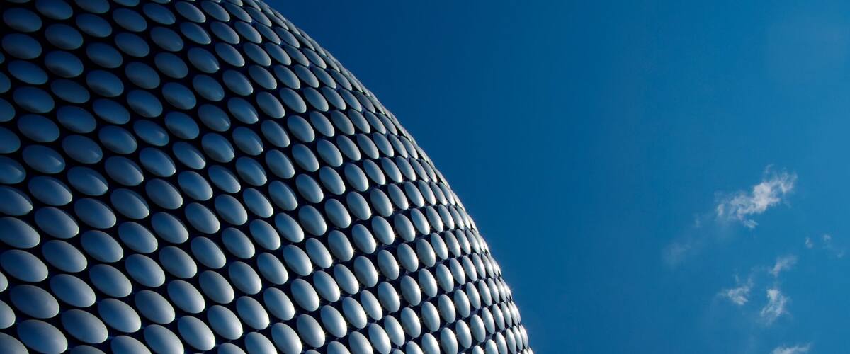 A modern architectural structure with a curved facade composed of numerous reflective, oval-shaped elements.