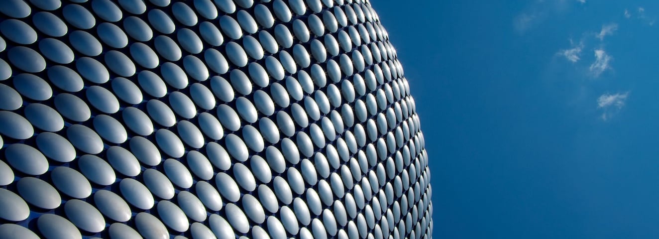 A modern architectural structure with a curved facade composed of numerous reflective, oval-shaped elements.