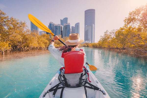 Une personne fait du kayak sur une rivière, avec la silhouette d’une ville en arrière-plan.