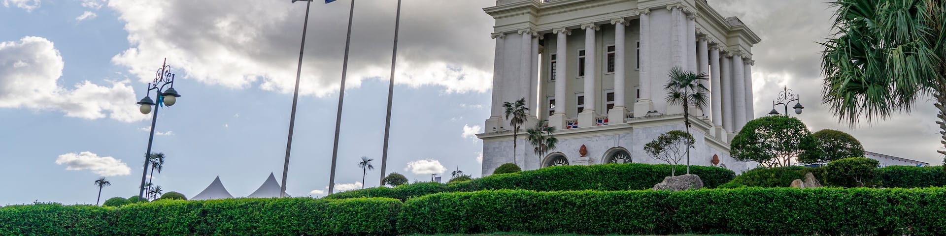 A tall monument with a statue on top, surrounded by lush greenery and palm trees.