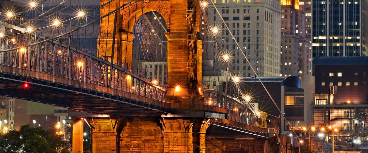 A historic bridge with illuminated lights, a prominent building with a green roof, and a modern skyscraper in the background.