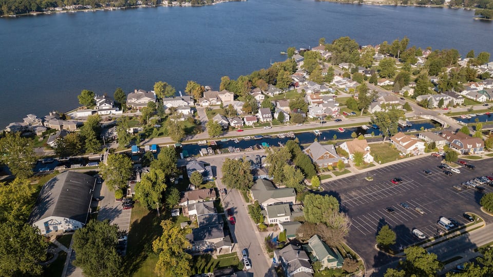 An aerial view of a lakeside residential area with houses, a bridge, and a parking lot.