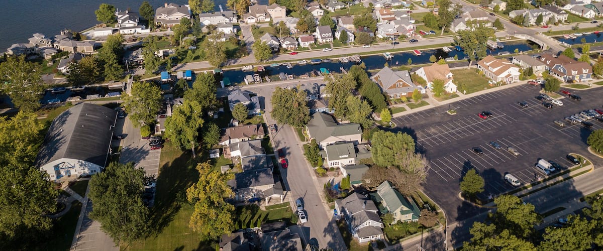 An aerial view of a lakeside residential area with houses, a bridge, and a parking lot.