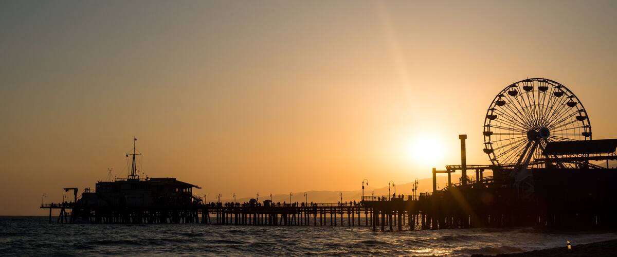 A pier with a Ferris wheel and a ship at sunset.