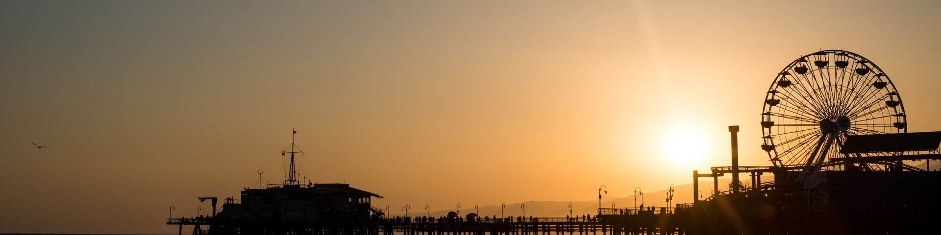 A pier with a Ferris wheel and a ship at sunset.