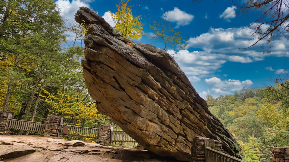 A large rock formation with a wooden fence in a forested area.