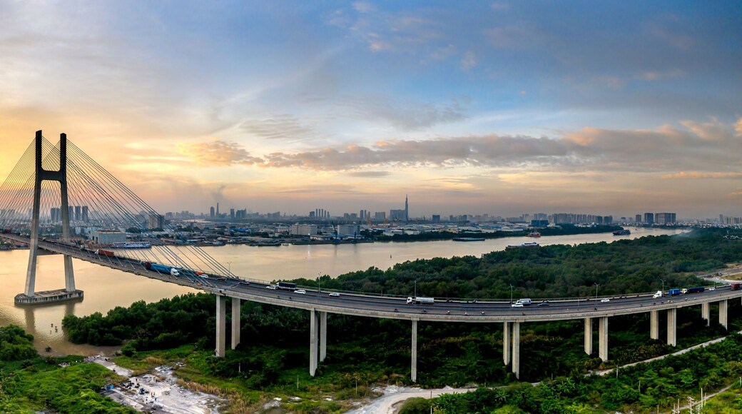 Eine Hängebrücke über einem Fluss, im Hintergrund die Skyline einer Stadt.