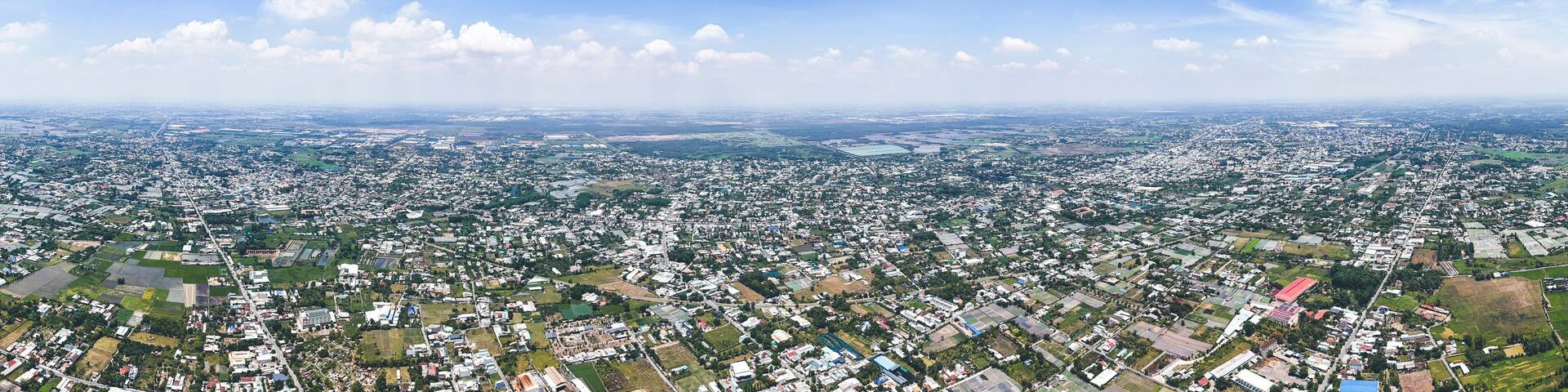A panoramic view of a densely populated city with a mix of residential and commercial buildings, green spaces, and a clear blue sky with scattered clouds.