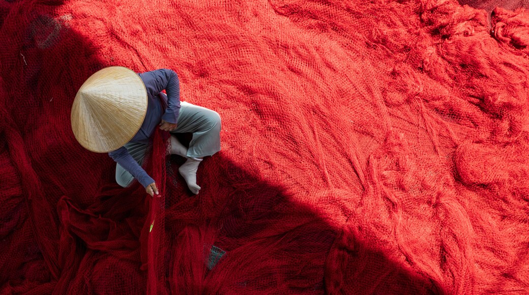 A person wearing a straw hat and blue clothing, working with red material.