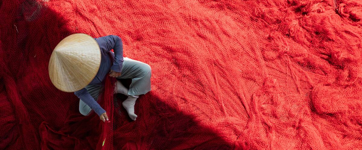 A person wearing a straw hat and blue clothing, working with red material.