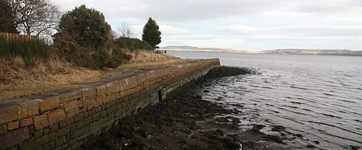 A waterfront with a brick wall, grassy area, and trees.