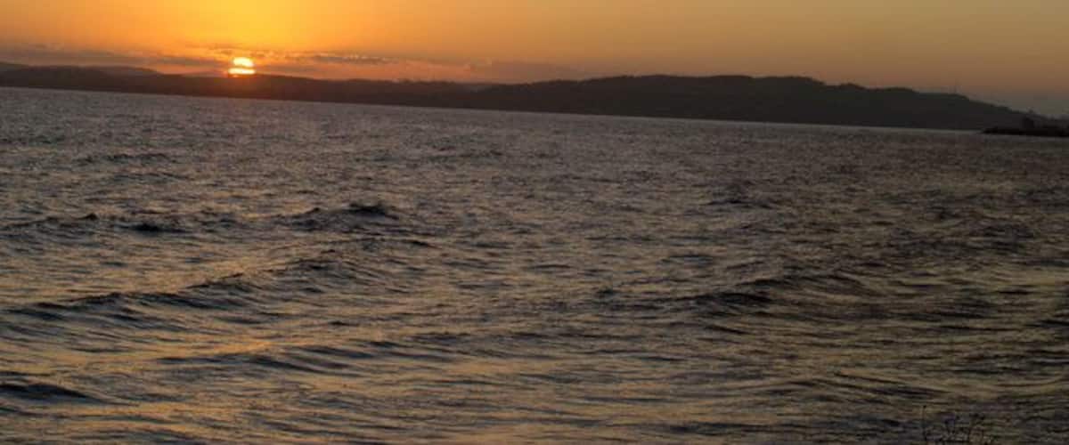 A sunset over a calm body of water with distant landforms.
