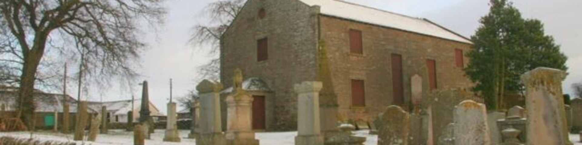 Uma igreja de pedra com um campanário, rodeada por um cemitério com lápides.