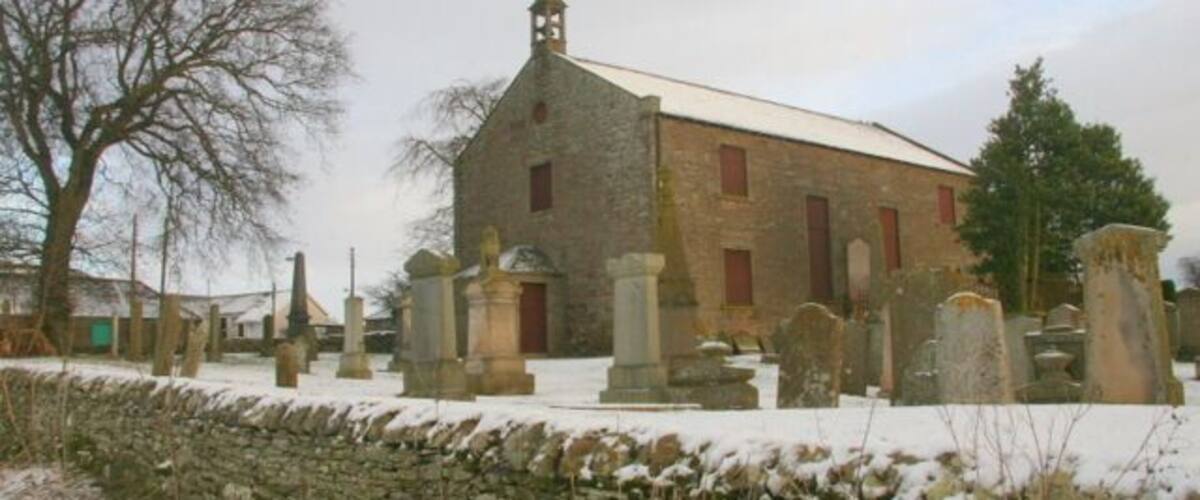 A stone church with a steeple, surrounded by a cemetery with headstones.
