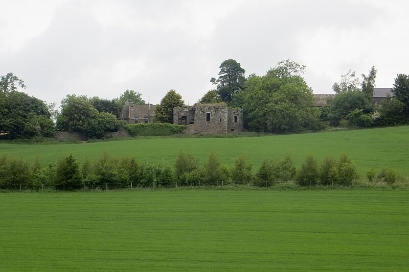 A green field with a stone building and trees in the background.